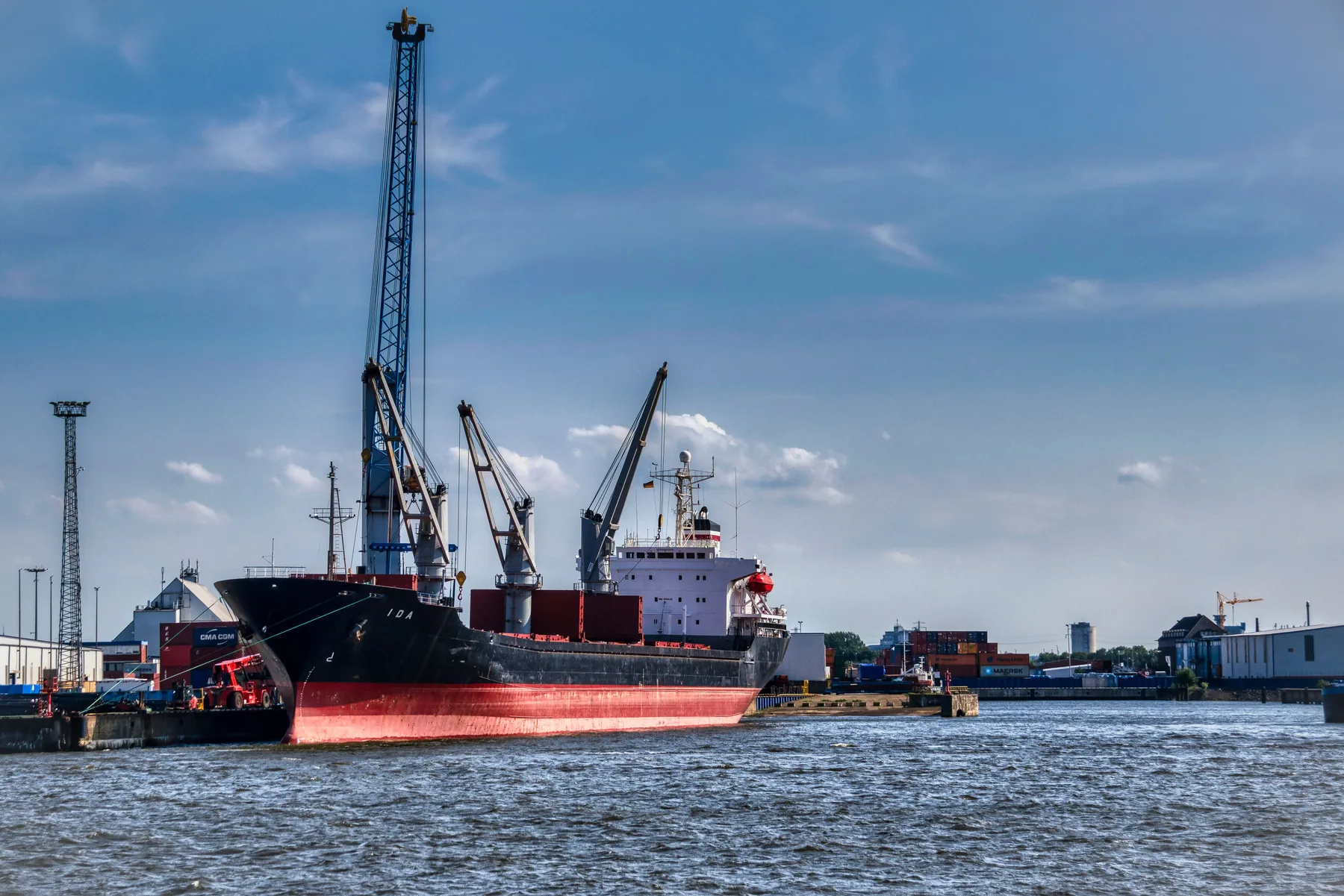 Large cargo vessel sailing on open water near an industrial port