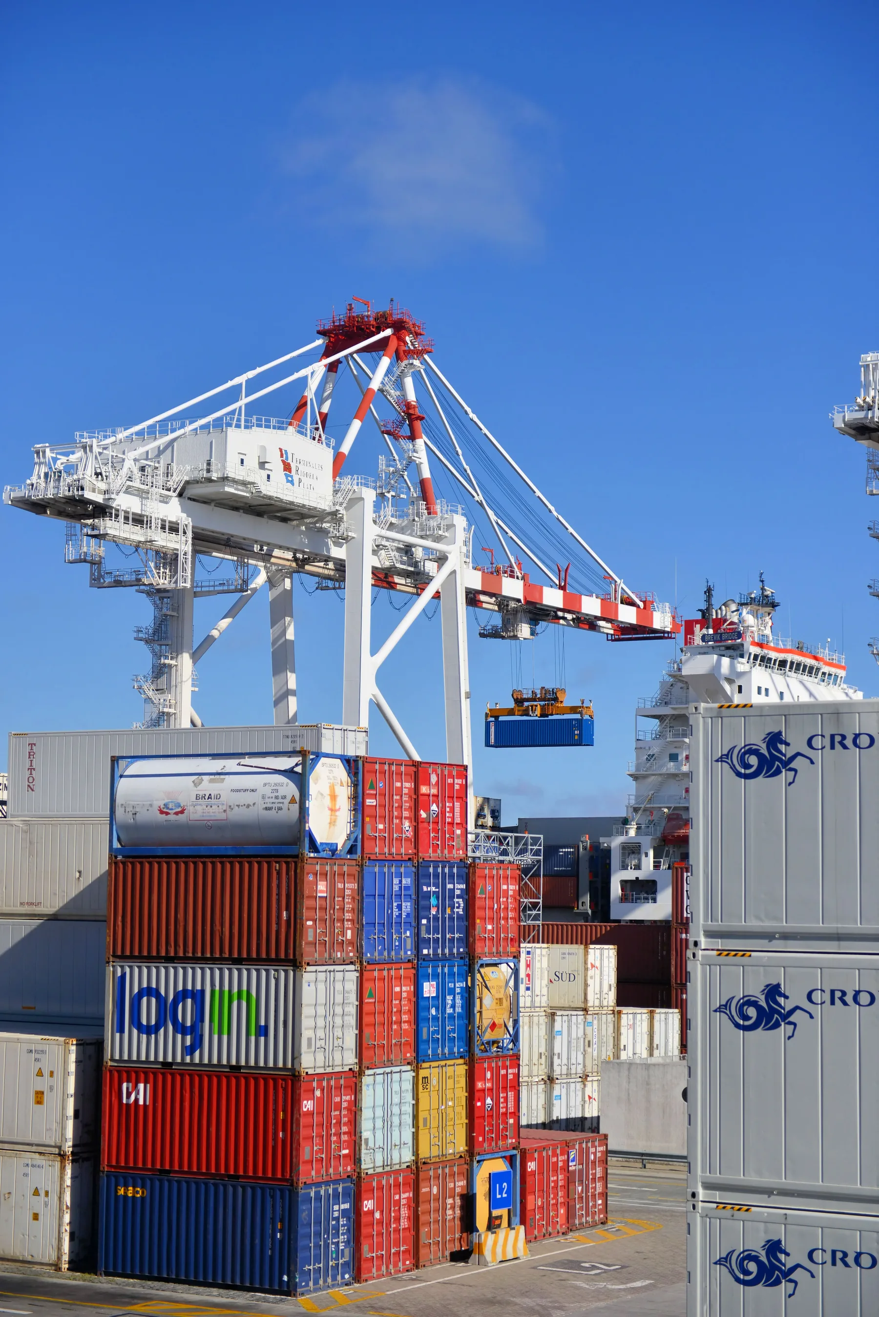 Port crane lifting a shipping container beside stacked cargo containers